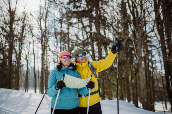 Senior couple looking at paper map during cross country skiing in snowy nature.