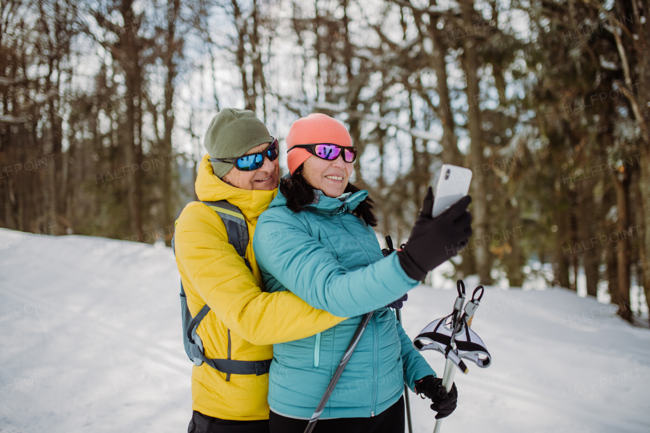 Senior couple taking selfie during cross country skiing in snowy nature.