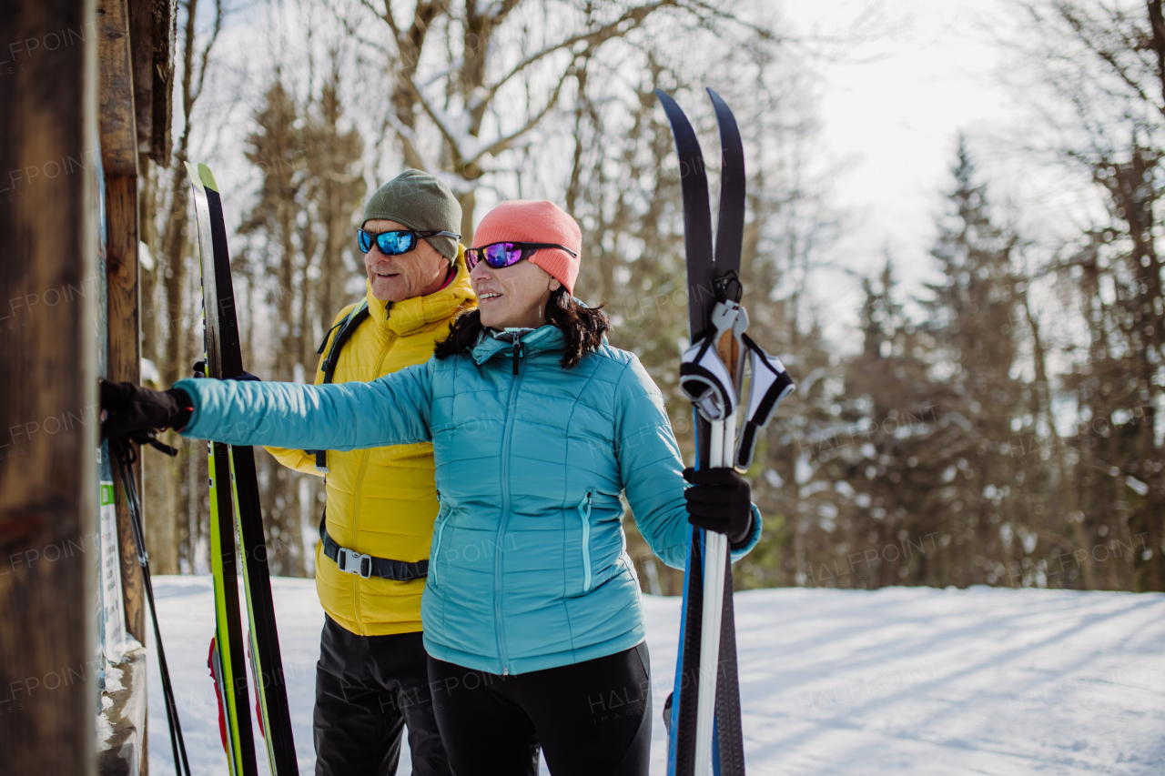 Senior couple looking at a tourist board in the middle of snowy forest.