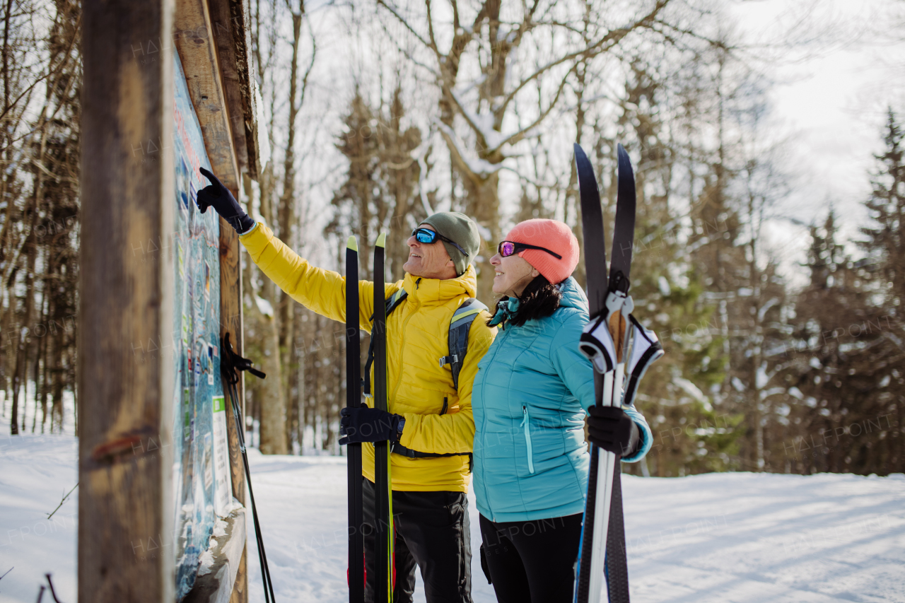 Senior couple looking at a tourist board in the middle of snowy forest.