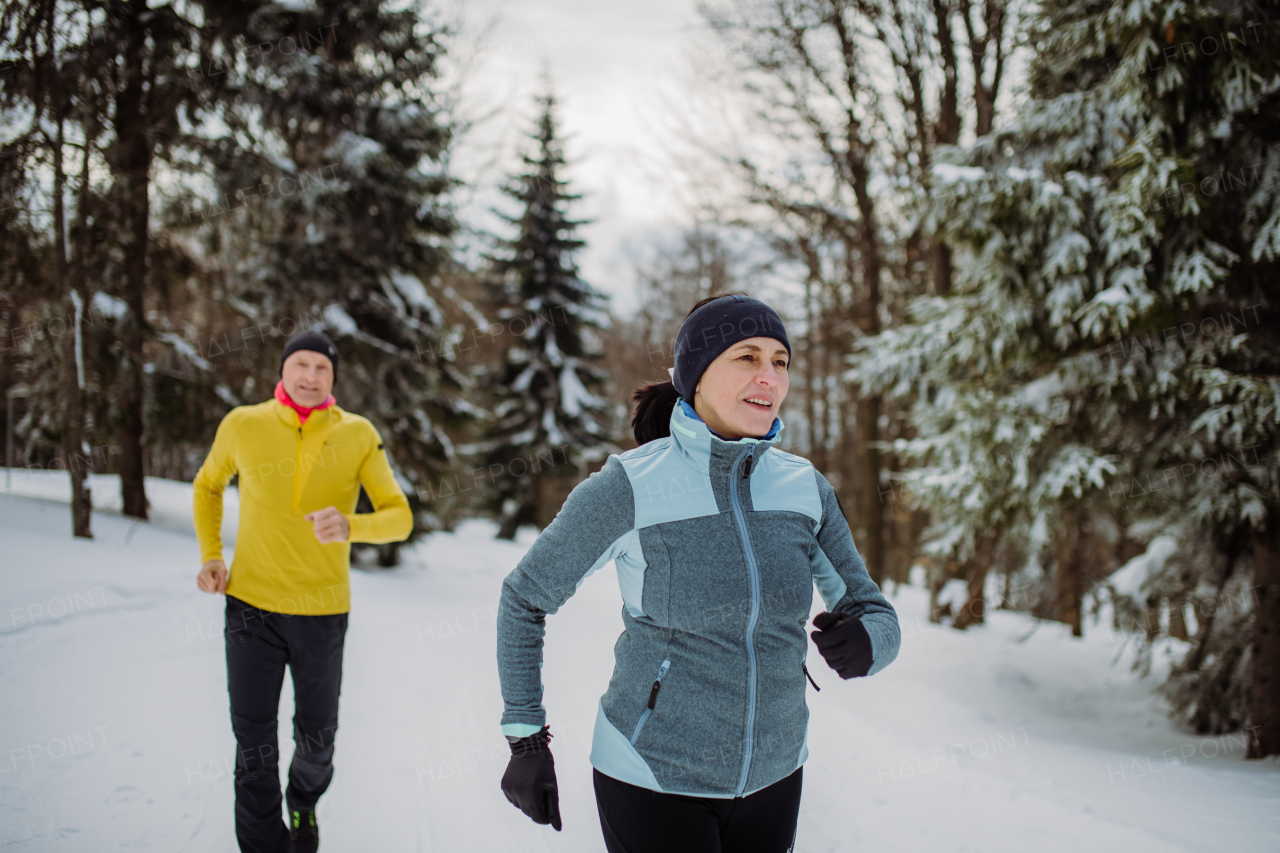 Senior couple jogging together in winter nature.