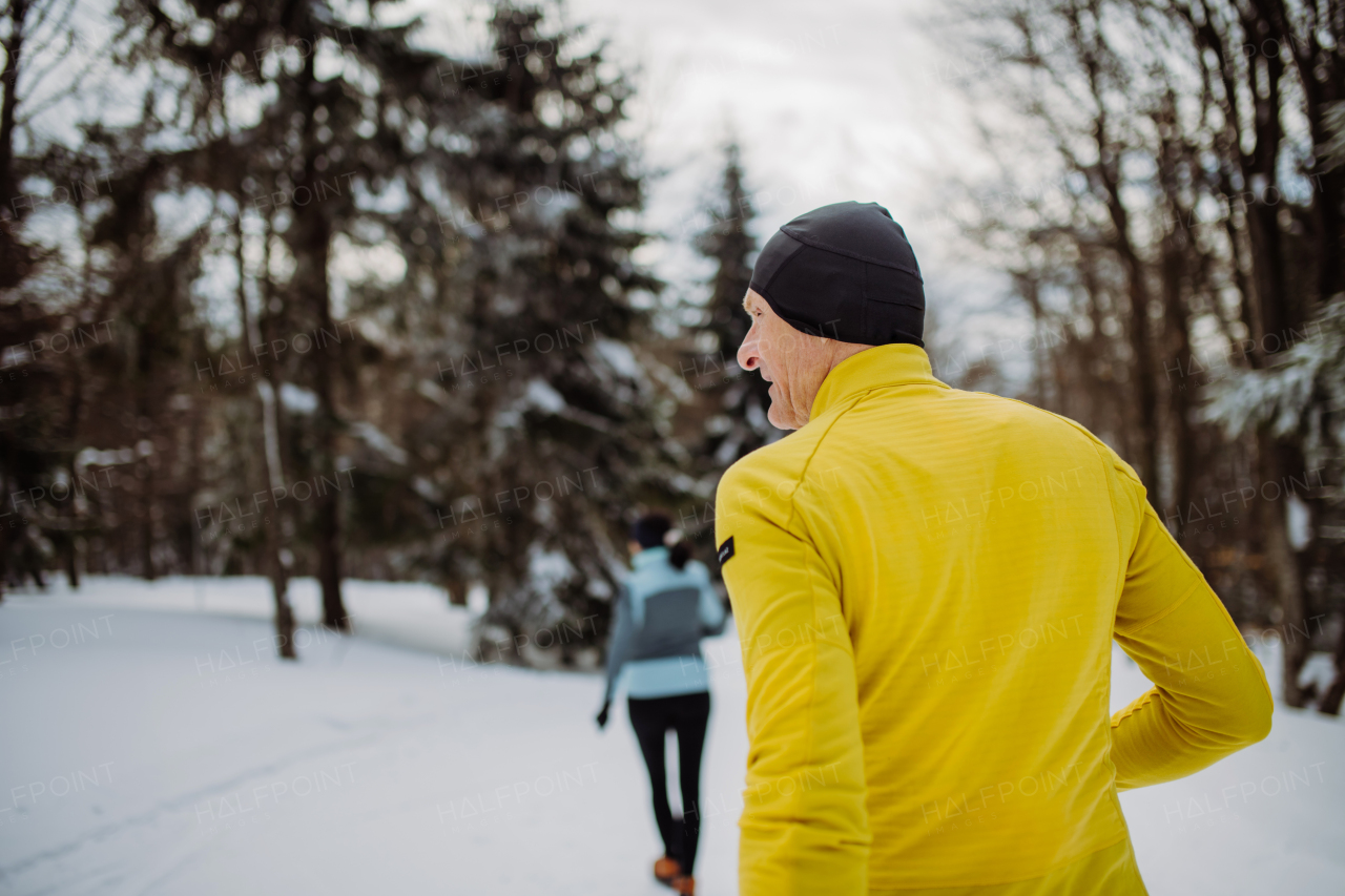 Senior couple jogging together in winter nature.