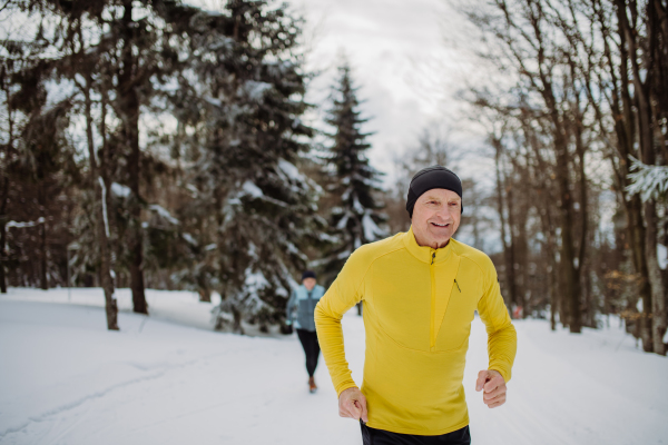 Senior couple jogging together in winter nature.