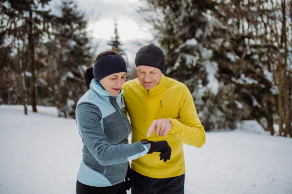 Senior couple looking at a smartwatch during winter run.