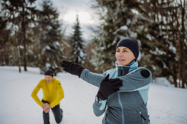 Senior couple warming-up and stretching in forest before winter hike.