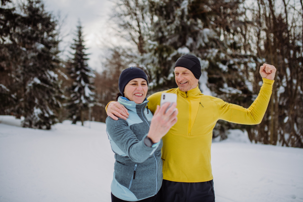 Senior couple taking selfie during jogging in snowy nature.