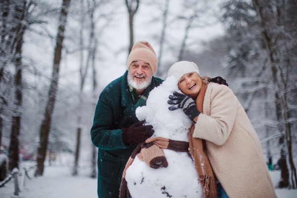 Elegant senior couple building snowman during cold winter snowy day. Elderly couple spending winter vacation in the mountains. Wintry landscape.