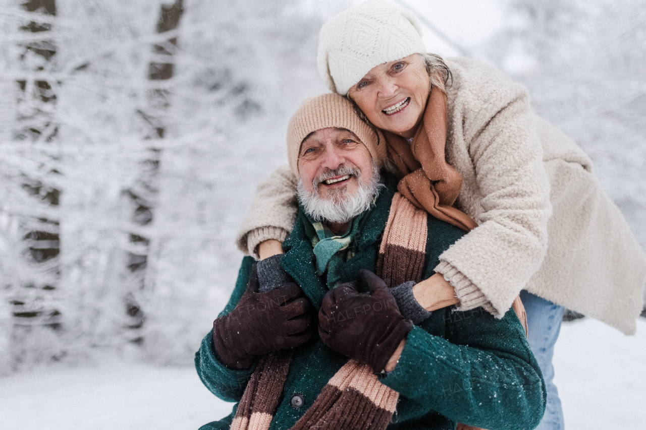 Close-up of elegant senior man with his wife in the snowy park, during cold winter snowy day. Elderly couple spending winter vacation in the mountains. Wintry landscape.