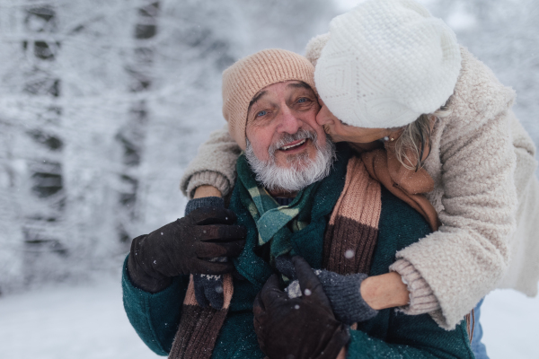 Close-up of elegant senior man with his wife in the snowy park, during cold winter snowy day. Elderly couple spending winter vacation in the mountains. Wintry christmas landscape.