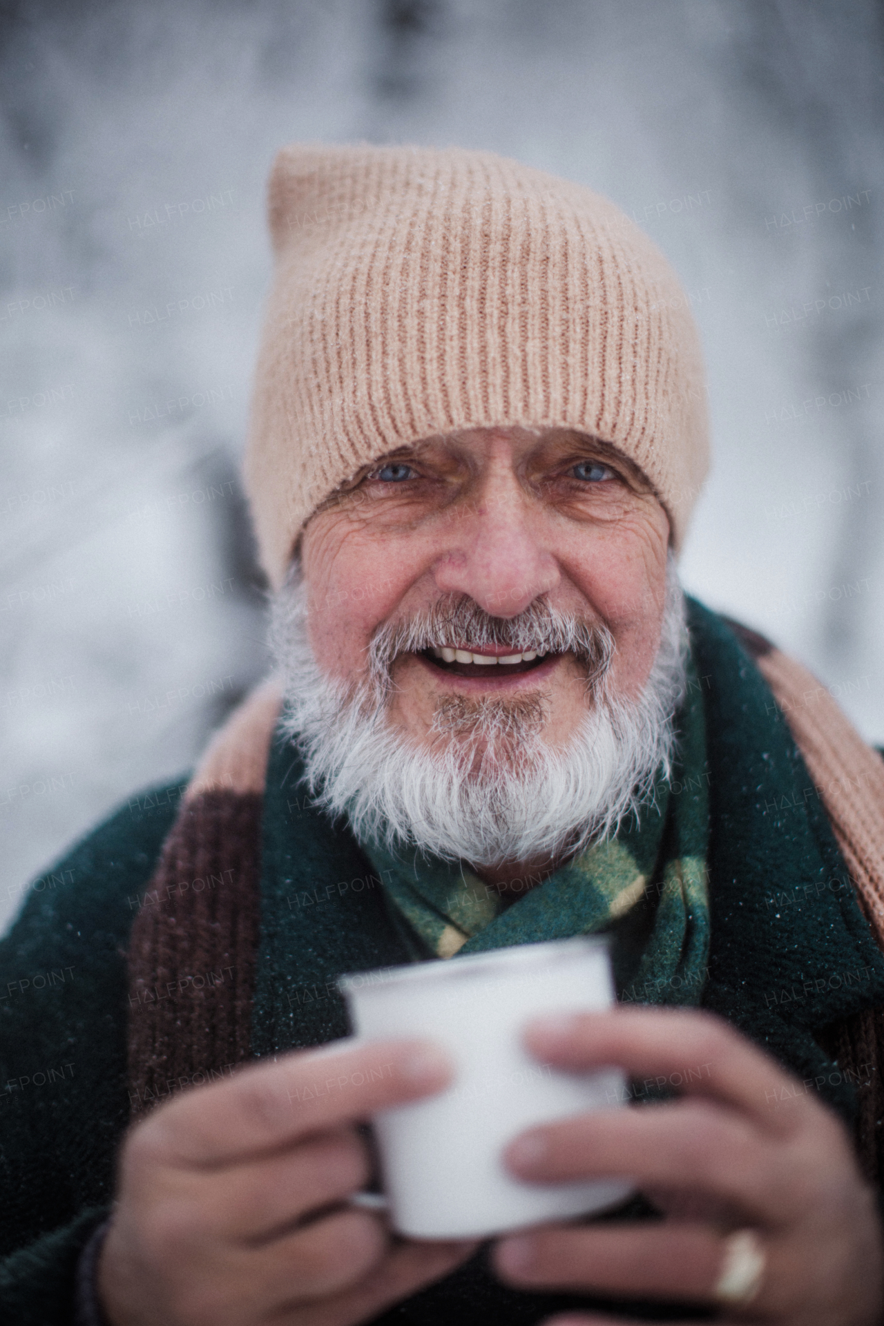 Portrait of elegant senior man drinking hot tea outdoors, during cold winter snowy day. Elderly man spending winter vacation in the mountains. Wintry landscape.