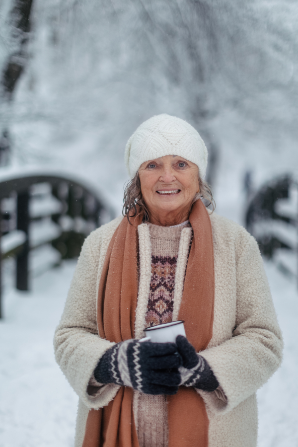 Portrait of elegant senior woman drinking hot tea outdoors, during cold winter snowy day. Elderly woman spending winter vacation in the mountains. Wintry christmas landscape.