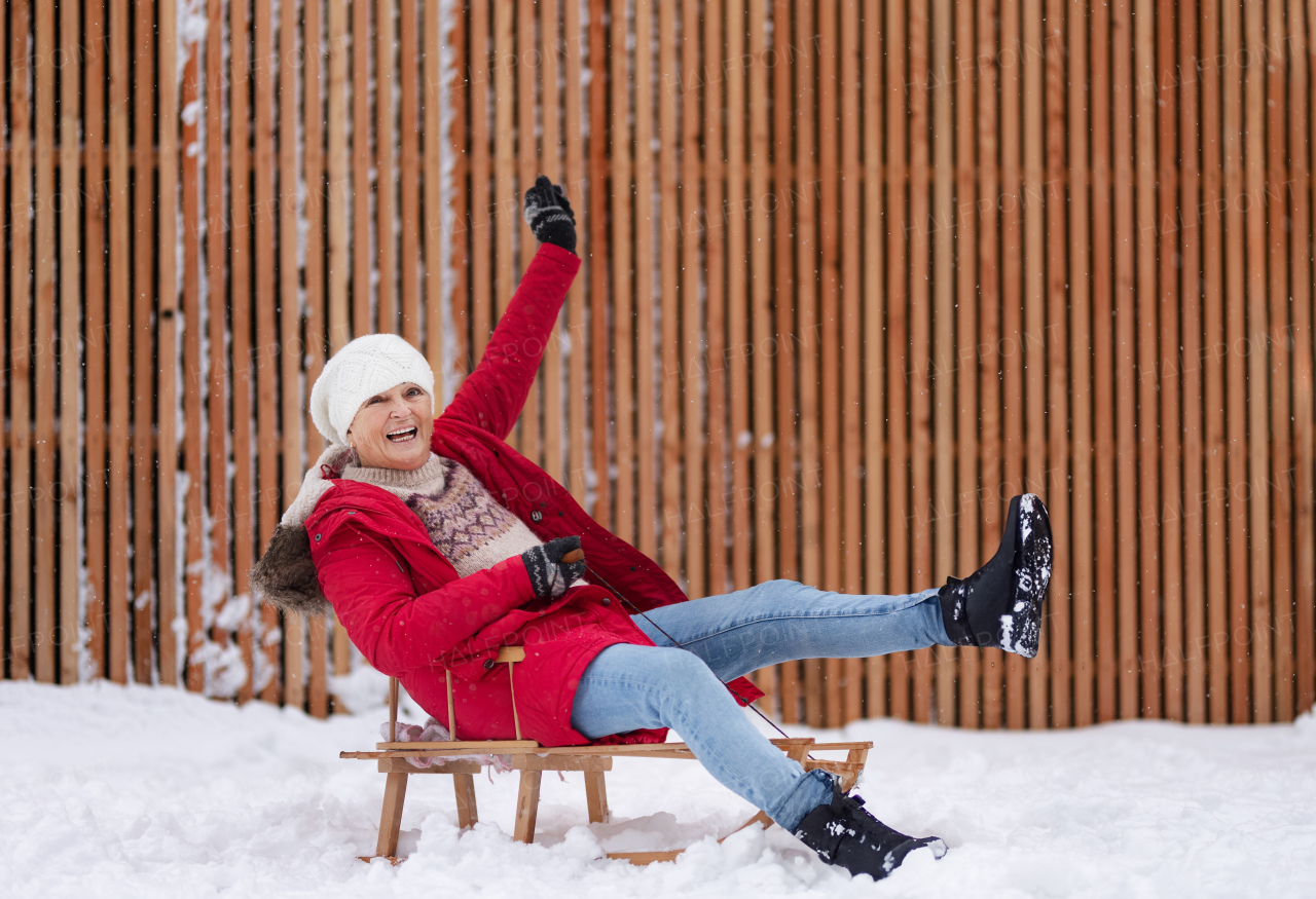 Senior woman having fun during cold winter day, sledding down the hill. Elderly woman spending winter vacation in the mountains. Wintry landscape.