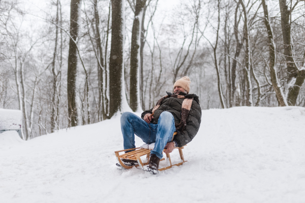 Senior man having fun during cold winter day, sledding down the hill. Elderly man spending winter vacation in the mountains. Wintry landscape.