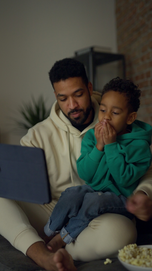 Young father with his son having a call on digital tablet, enjoying time together. Vertical view.