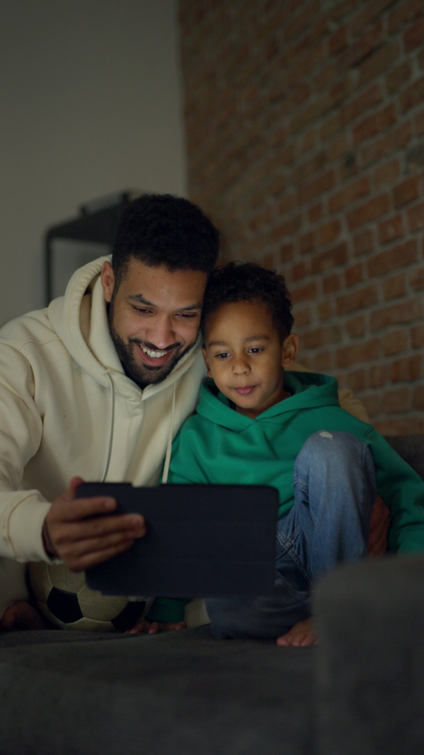 Young father with his looking something on digital tablet, enjoying time together. Vertical view.