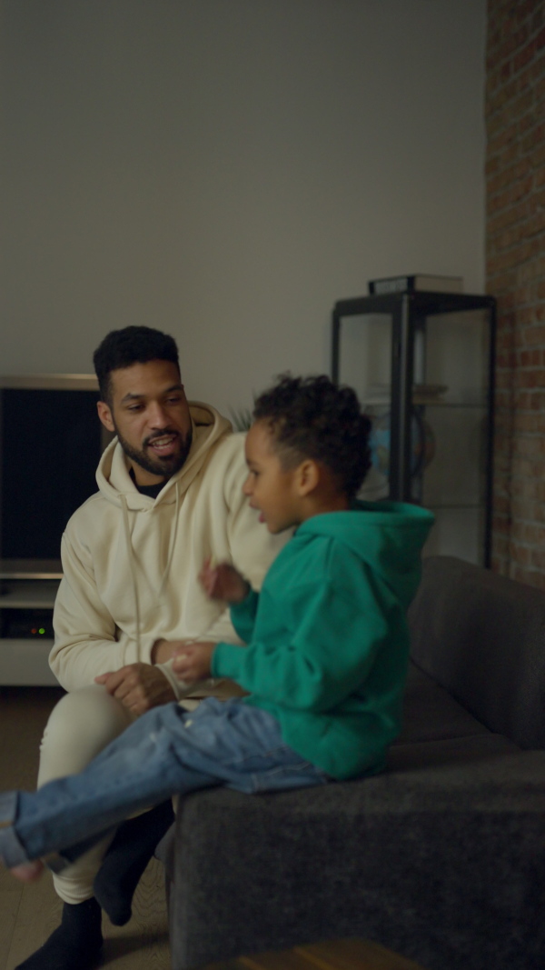 Multiracial father and his son having fun in their apartment. Vertical view.