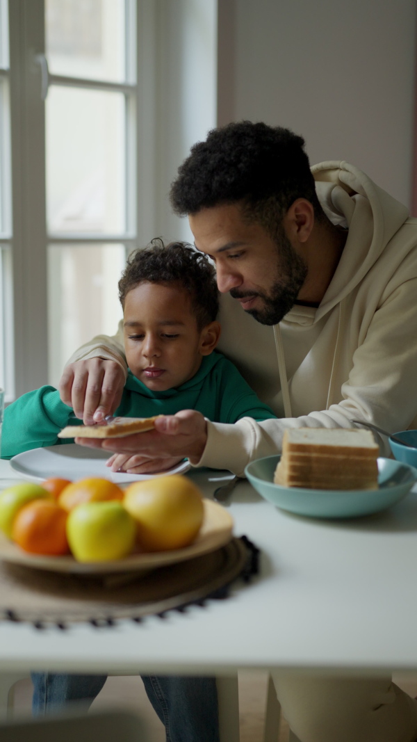 Young father and his little son having breakfast together in their flat. Vertical view.