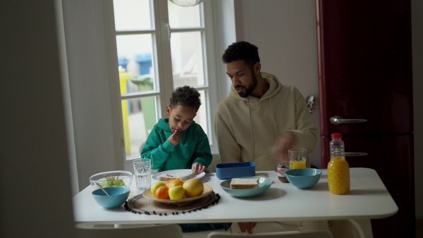 Young father and his little son having breakfast together in their flat.