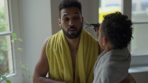 Young father showing his little son how to shave beard, having fun together.