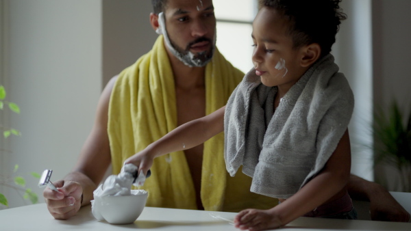 Young father showing his little son how to shave beard, having fun together.