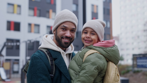 Young father and his little son during outdoor walk in a city, holding him and looking at camera.