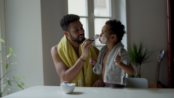 Young father showing his little son how to shave beard, having fun together.