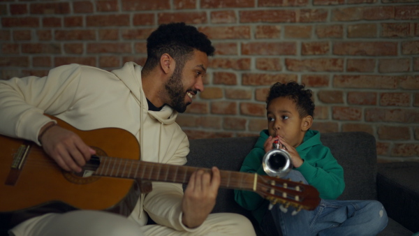 Father and son playing on musical instruments in their living room, having fun together.