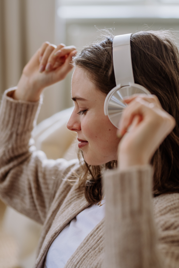 Young woman listening music trough headphones in the apartment.