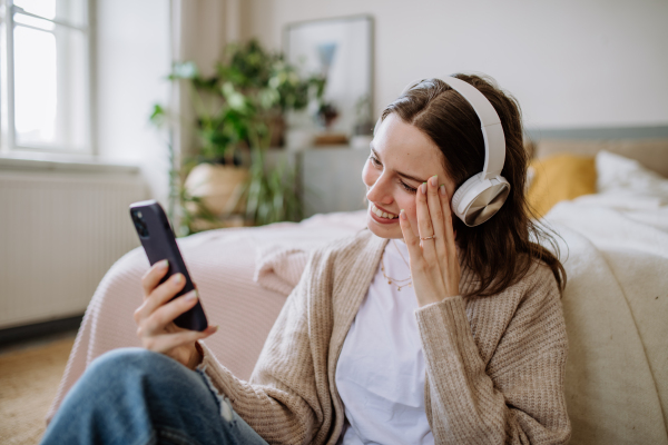 Young woman listening music trough headphones in the apartment.