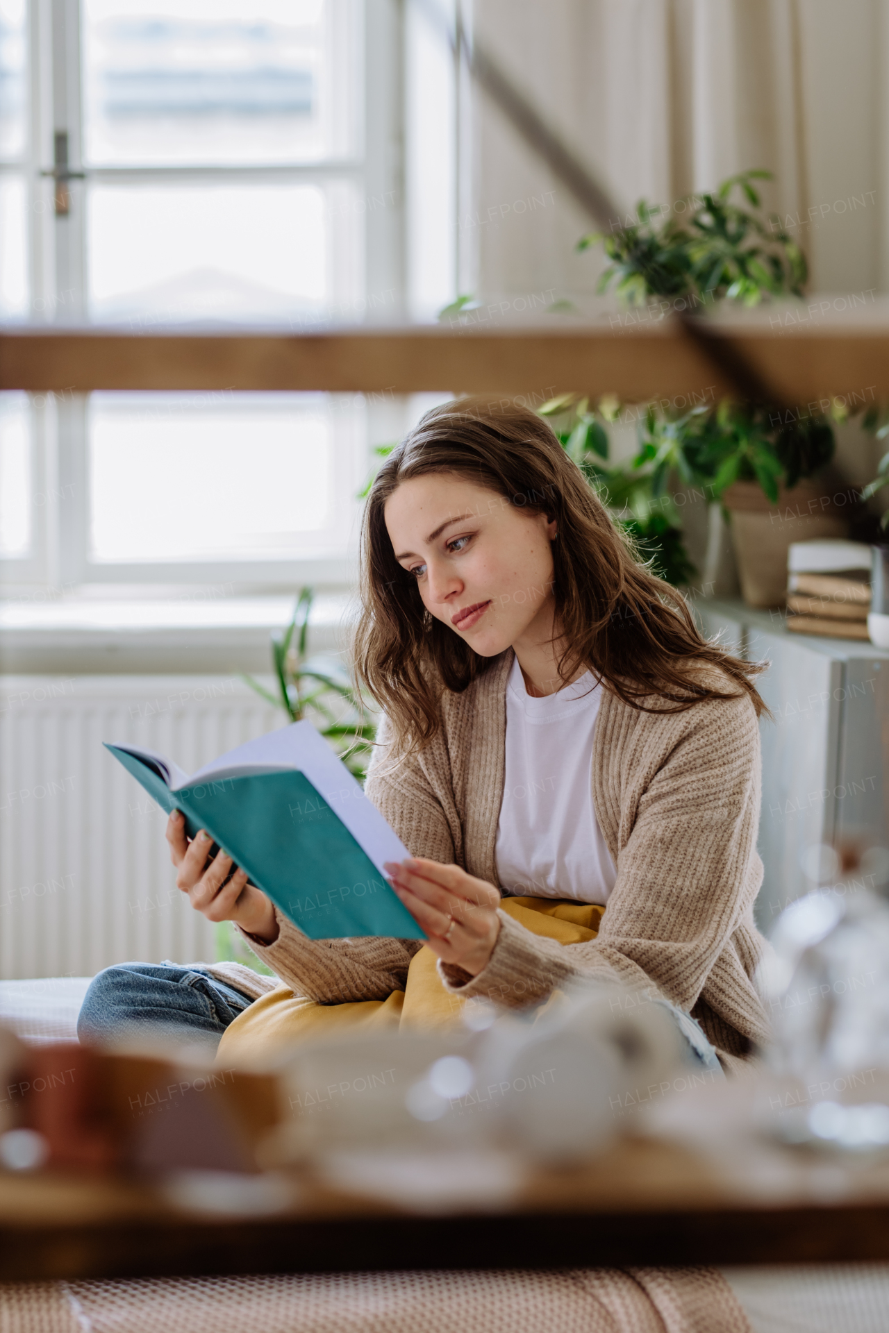 Young woman enjoying leisure time in her apartment, reading a book.