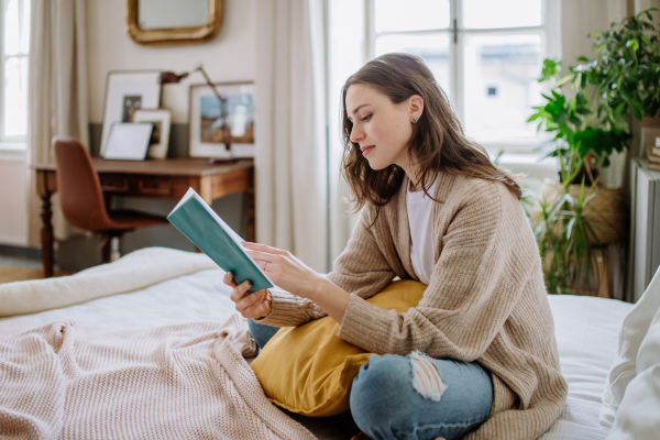 Young woman enjoying leisure time in her apartment, reading a book.