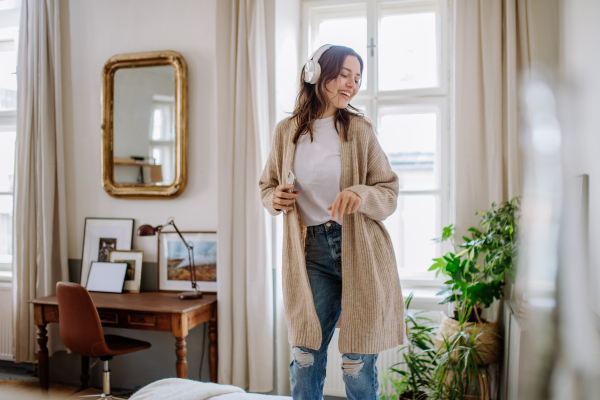 Young woman listening music trough headphones in the apartment.