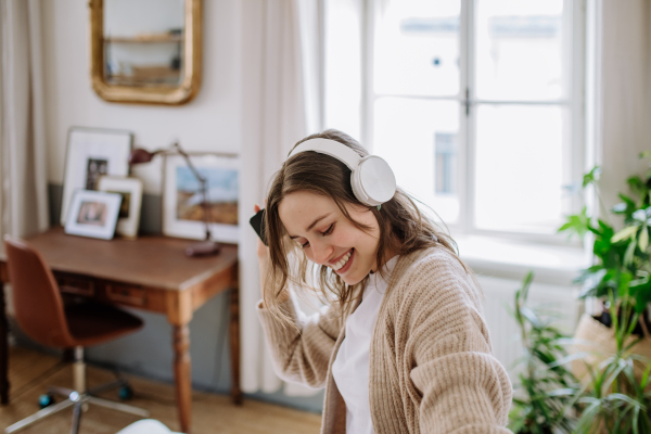 Young woman listening music trough headphones in the apartment.