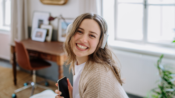 Young woman listening music trough headphones in the apartment.