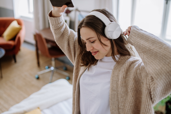 Young woman listening music trough headphones in the apartment.