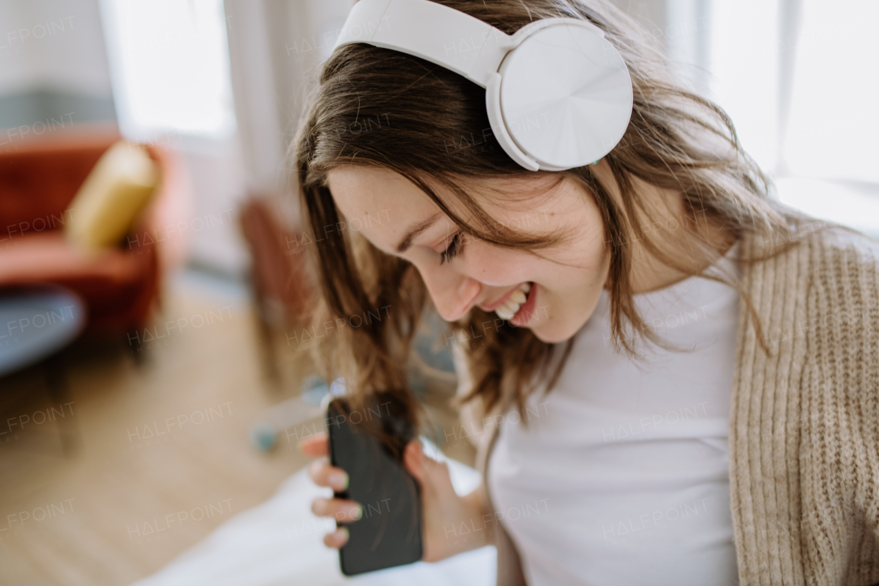 Young woman listening music trough headphones in the apartment.