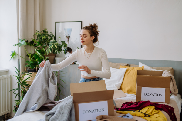 Young woman giving her clothes packed in box to charity.