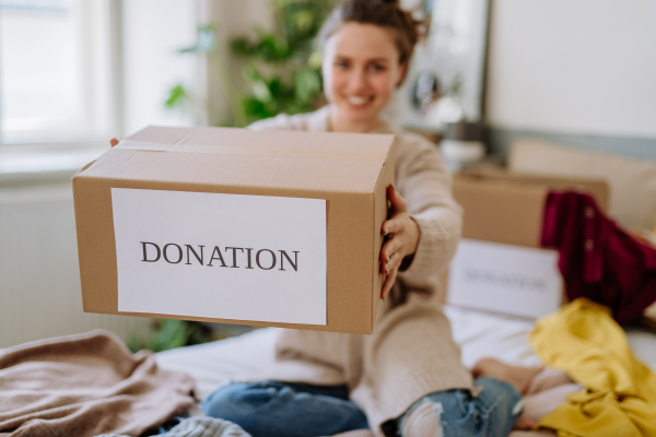 Young woman giving her clothes packed in box to charity.