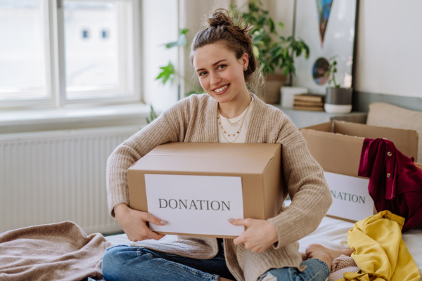 Young woman giving her clothes packed in box to charity.