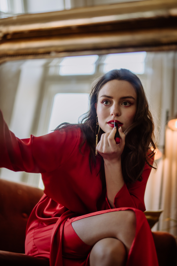 Young woman in elegant dress preparing for an evening, finishing her make up.