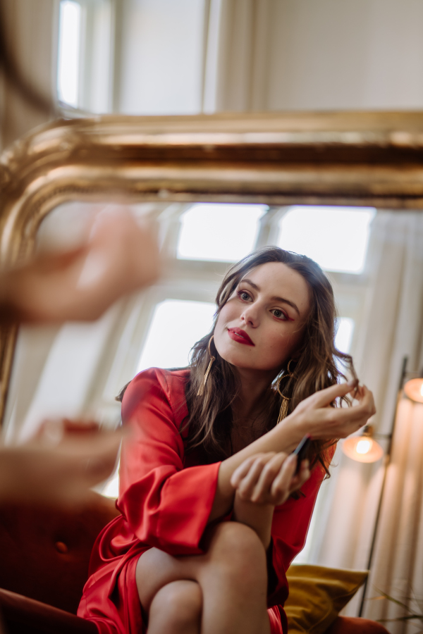 Young woman in elegant dress preparing for an evening, looking in a mirror.