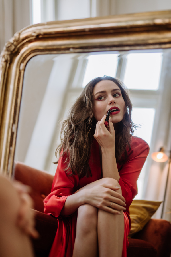 Young woman in elegant dress preparing for an evening, finishing her make up.