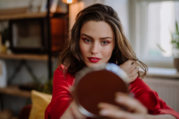 Young woman in elegant dress preparing for an evening, finishing her make up.