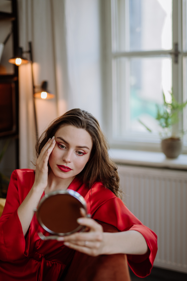 Young woman in elegant dress preparing for an evening, finishing her make up.