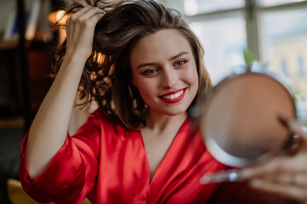 Young woman in elegant dress preparing for an evening, looking in a mirror.