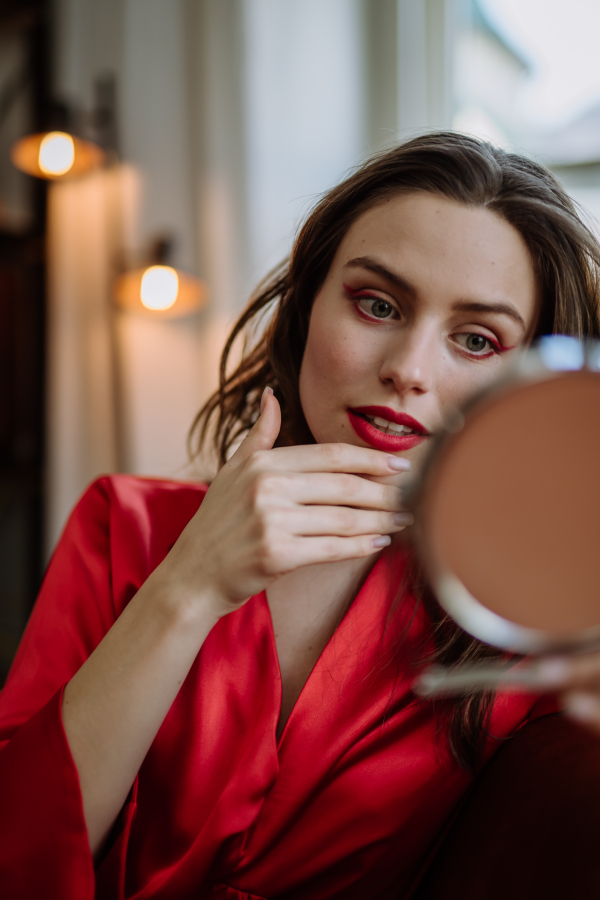 Young woman in elegant dress preparing for an evening, finishing her make up.