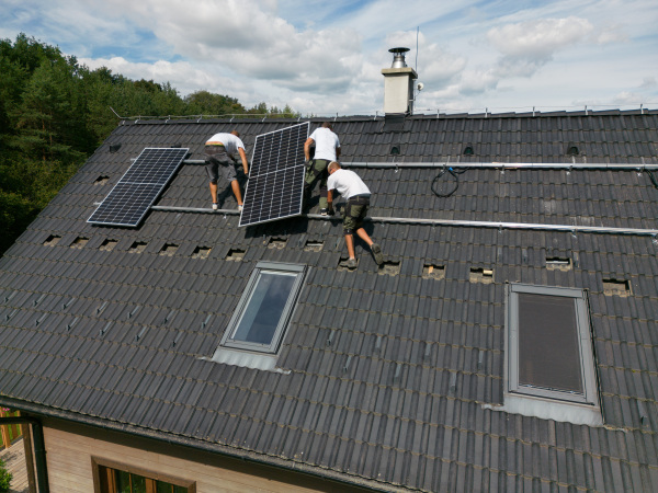 Men worker installing solar photovoltaic panels on a roof, alternative energy, saving resources and sustainable lifestyle concept.