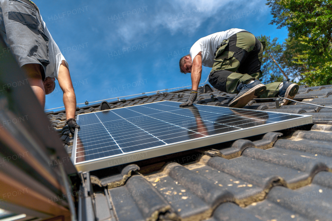 Men worker installing solar photovoltaic panels on a roof, alternative energy, saving resources and sustainable lifestyle concept.