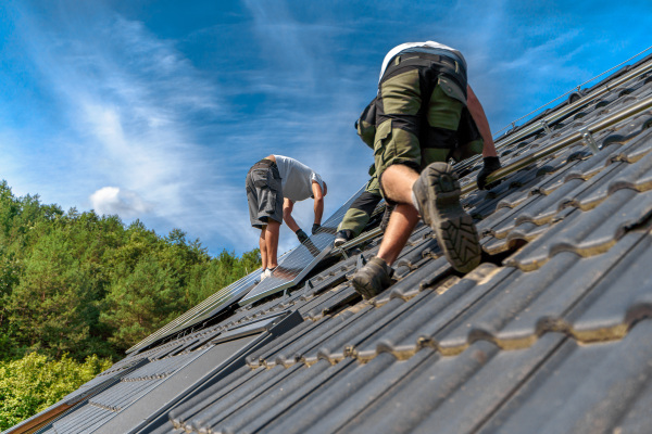 Men worker installing solar photovoltaic panels on a roof, alternative energy, saving resources and sustainable lifestyle concept.