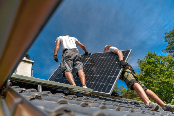 Men worker installing solar photovoltaic panels on a roof, alternative energy, saving resources and sustainable lifestyle concept.